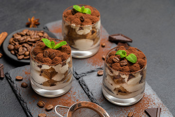 Classic tiramisu dessert in a glass on stone serving board on dark concrete background
