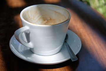 Empty cappuccino cup with a silver colored spoon is standing on a wooden table