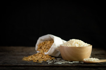 Closeup of rice seeds in wooden bowl with blurred paddy rice in sack on old wooden board