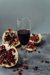 A wine glass with red wine stands on a gray grunge background next to grenades. Fruits and pomegranate wine
