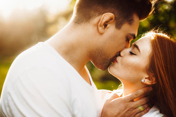 Fototapeta premium Close up portrait of a amazing caucasian female with freckles and red hair kissing with her boyfriend outside against sunset while traveling.