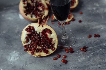 A glass of wine on a gray background among pomegranates. Close pomegranate and red pomegranate seeds.