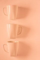 3 Orange coffee mugs on orange background in a vertical row with empty copyspace