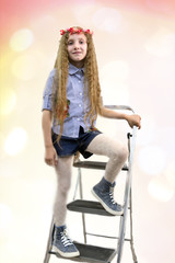 Positive teen girl with long hair and wreath on her head is standing on a stepladder