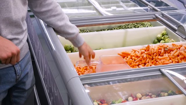 man buys carrot in the mall. a young guy picks up frozen carrot Selection of Frozen Close- up