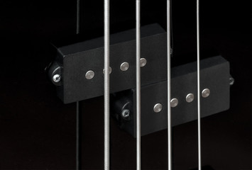 Close-up bass guitar pickups and strings. Musical instruments. Black guitar deck.
