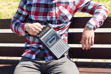 Hipster fancy man in plaid shirt holding in hand and walking with retro vintage old 80s , 90s style portable radio audio cassette recorder player boombox with audio tape cassette inside 