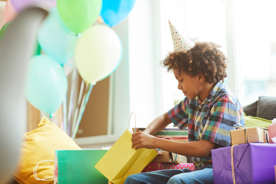 Side View Portrait Of Happy African-American Boy Opening Presents At Birthday  Party, Copy Space