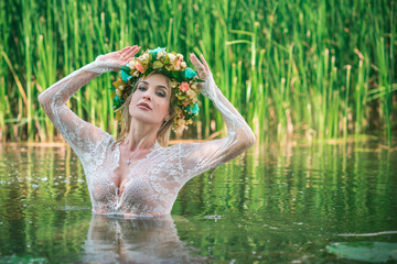 Fototapeta premium A fabulous, lake nymph in long white lace dress and wreath. Artistic Photography, Mysterious scene. European Witch . Fairytale