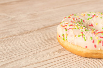 Fresh glazed donut with colorful sprinkles on a wooden table.