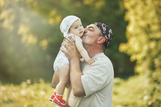 Young Grandfather Playing With Adorable Baby Girl Over A Nature Background. Grandparents And Grandchild Leisure Time Concept.