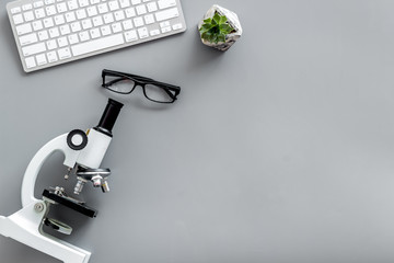 Do medical research on laboratory desk with microscope, keyboard, glasses on gray background top view mockup