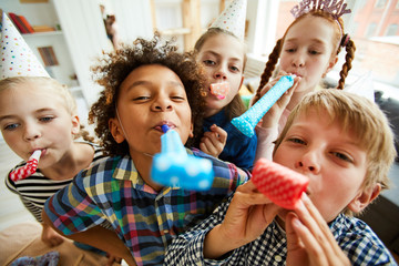 High angle view at multi ethnic group of children blowing party horns at camera - Powered by Adobe