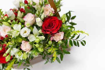 emotional composition of fresh flowers, greenery and berries (green, light green with white and bright red accents) in a wooden box with a rope handle on a light background