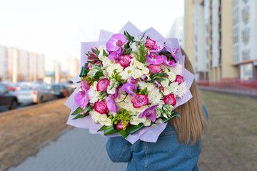 A bright bouquet of white roses and exotic flowers (white, red, burgundy, green) in the hands of a young girl on a city street