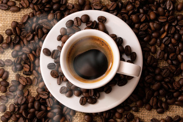 A cup of fresh coffee on burlap. A scattering of coffee beans with a cup of coffee. Coarse fabric.