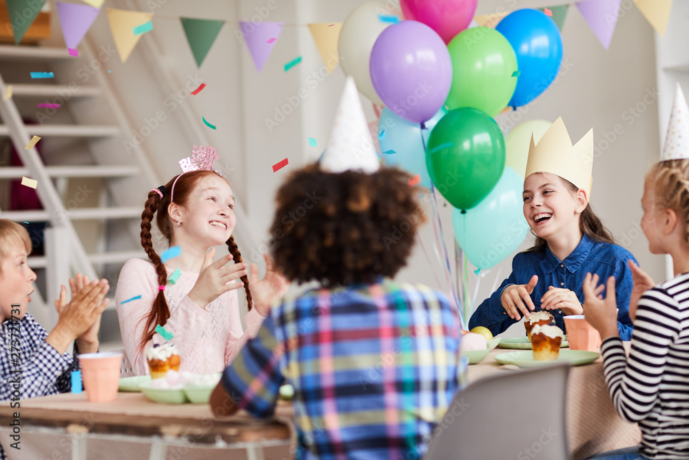 Wall mural Group of happy children having fun during Birthday party in decorated room with confetti, copy space