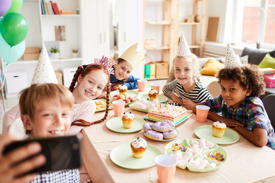 Multi ethnic group of children taking selfie during fun Birthday party in decorated room, copy space