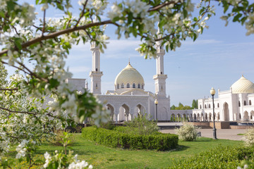 Fototapeta na wymiar White mosque of the Bulgarians on a sunny spring day against the backdrop of blossoming apple tree branchesapple are out of focus