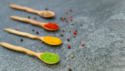 Spices lie in wooden spoons on a black background, top view, soft focus. Spices and seasonings for cooking in the composition on the table.