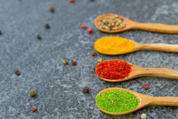 Spices lie in wooden spoons on a black background, top view, soft focus. Spices and seasonings for cooking in the composition on the table.