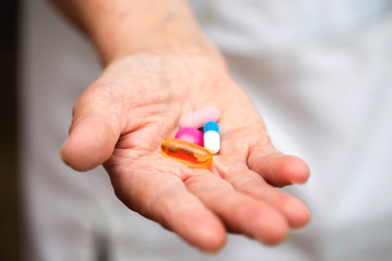 Many multi-colored pills in a Senior's hands. Painful old age. Caring for the health of the elderly