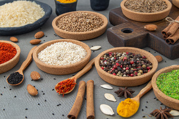 Spices lie in bowls and wooden spoons on a gray background , top view, soft focus. Spices and seasonings for cooking in the composition on the table.