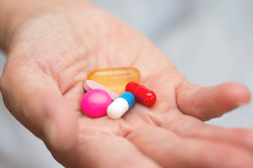 Many multi-colored pills in a Senior's hands. Painful old age. Caring for the health of the elderly