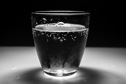 Low key image of round glass filled with sparkling water, on the white surface, with black background. Hydration concept.