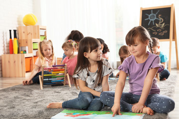 Cute girls reading book on floor while other children playing together in kindergarten