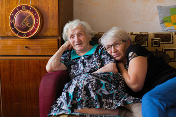 Russian old woman with her adult daughter sitting together at home watching on TV Putin's speech.