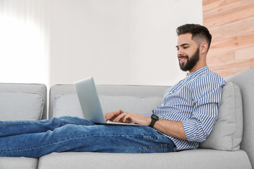 Handsome young man working with laptop on sofa at home