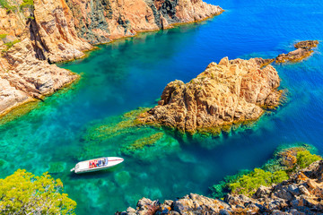 White motorboat in beautiful sea cove of Cala Marquesa with green pine trees on high rock cliffs,...