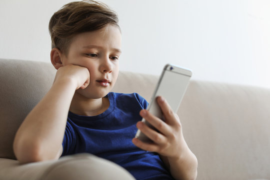 Little child with smartphone on sofa in room. Danger of internet