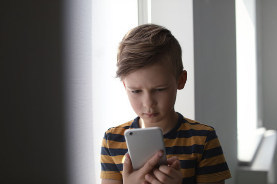 Sad little child with smartphone indoors. Danger of internet