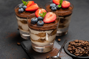 Classic tiramisu dessert with blueberries and strawberries in a glass on stone serving board on dark concrete background
