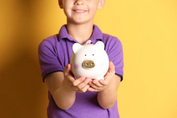 Fototapeta na wymiar Little boy with piggy bank on color background, closeup
