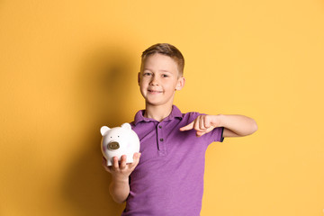 Fototapeta na wymiar Little boy with piggy bank on color background