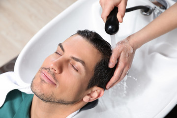 Obraz na płótnie Canvas Stylist washing client's hair at sink in beauty salon