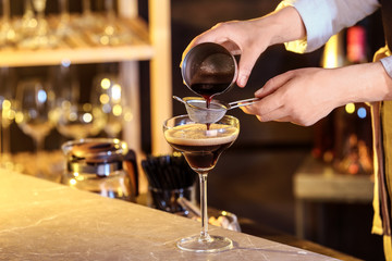 Woman preparing Espresso Martini on bar counter, closeup. Alcohol cocktail