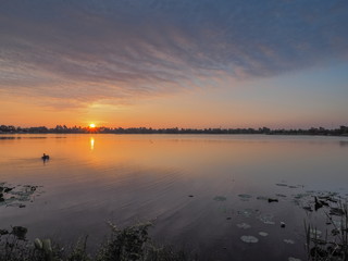 Lake view morning scenic a fisherman floating in water with red sun light and blue sky background, sunrise at Krajub Lake, Ban Pong, Ratchaburi, Thailand.