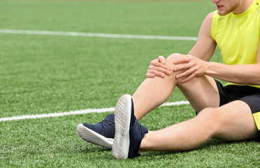 Man in sportswear suffering from knee pain at soccer field, closeup