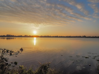 Lake view morning scenic a fisherman floating in water with red sun light and blue sky background, sunrise at Krajub Lake, Ban Pong, Ratchaburi, Thailand.
