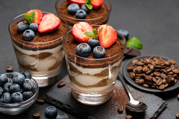 Classic tiramisu dessert with blueberries and strawberries in a glass on stone serving board on dark concrete background