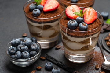 Classic tiramisu dessert with blueberries and strawberries in a glass on stone serving board on dark concrete background