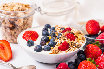 White yogurt in bowl with oatmeal and strawberries, blueberries and raspberries on the top on white background.