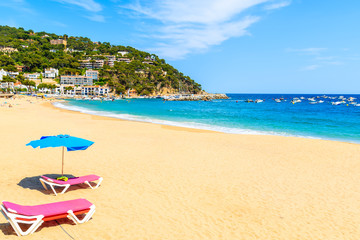 Sunbeds with umbrella on sandy beach in Llafranc village, Costa Brava, Spain
