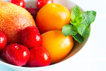 Fruit in a bowl. Red cherry, apricots, Forelle pear with fresh mint in a white bowl.