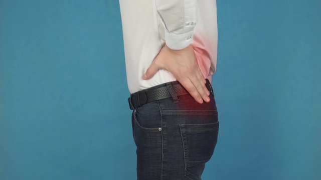 Pain in the muscle of the lumbar region or lower back spine, radiculitis concept due to long-term work at the computer. A man in a white shirt suffers from lumbago in the nerves and bones of the back