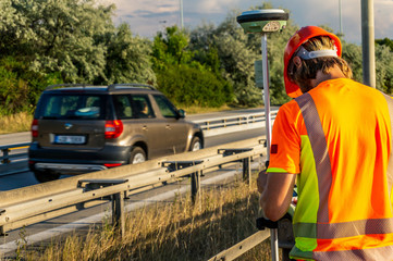 Surveyor engineer or worker with GPS on construction site during the sunny day with road or highway in background